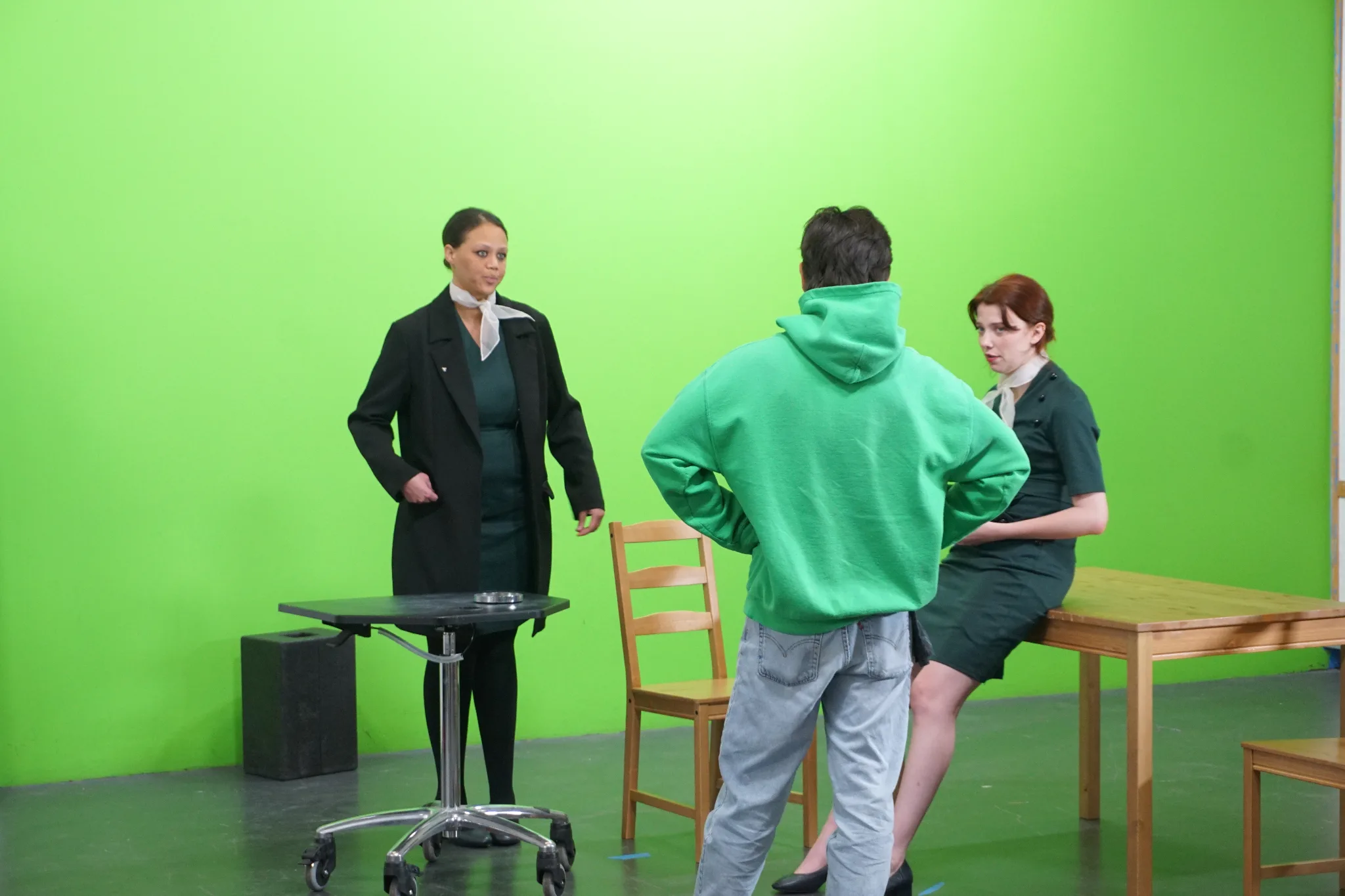 On-set production photo: actors performing under flat, even lighting with multiple cameras.
